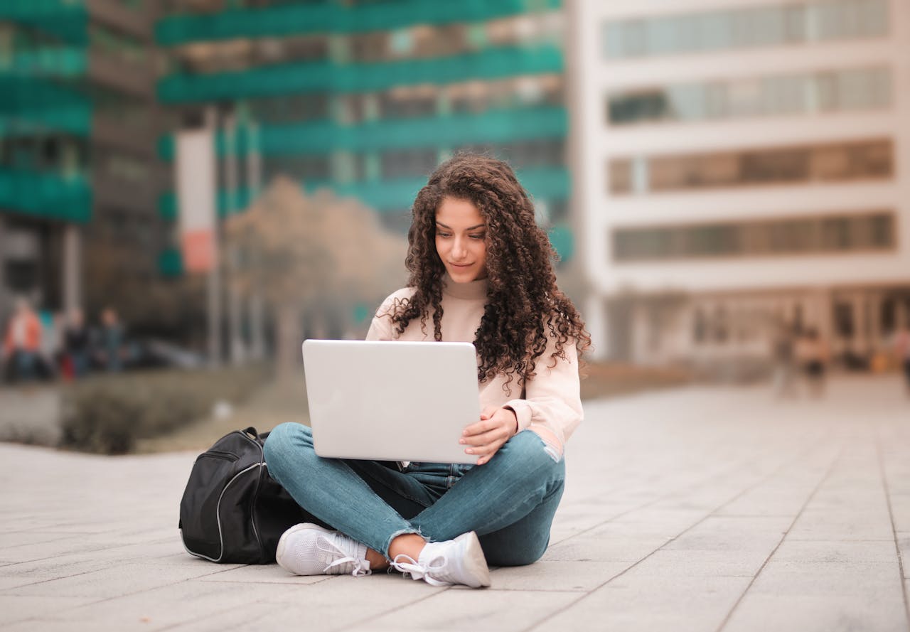 A woman with curly hair using a laptop while sitting outdoors, showcasing modern remote work lifestyle.